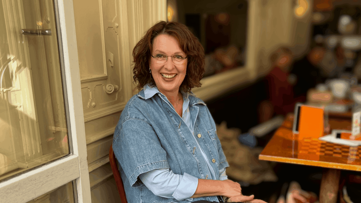 Frau sitzt im Cafe und lacht optimistisch in die Kamera.