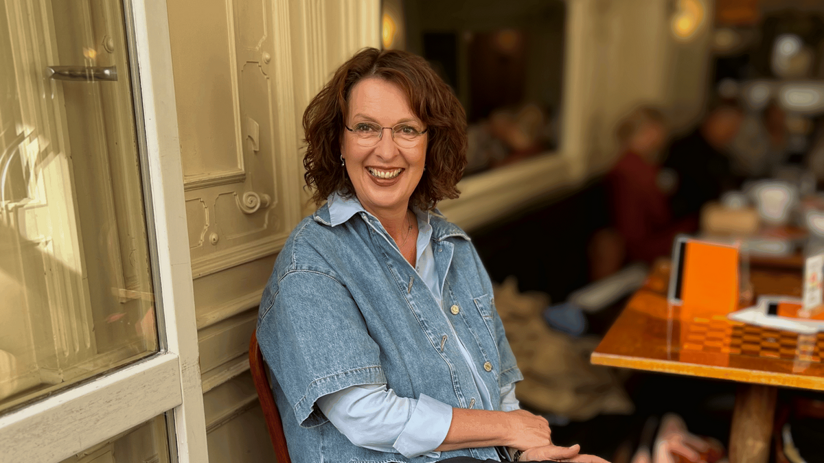 Frau sitzt im Cafe und lacht optimistisch in die Kamera.